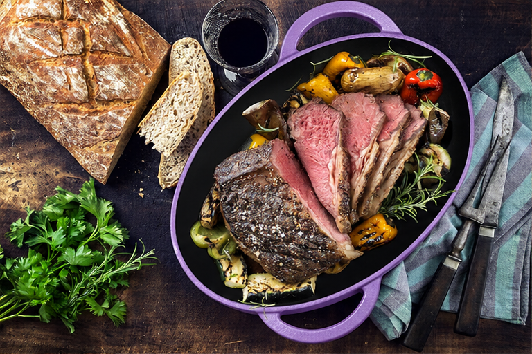 Laad de afbeelding in de galerijviewer, OSTOVE emaillierter ovaler Gusseisenbräter in Violett mit angerichtetem Braten # Farbe_Violett
